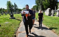 A.J. Orlikoff, Director of Programming at Historic Congressional Cemetery, leads attendees on a guided tour and places a commemorative flag at the final resting place of each identified D.C. Militia member buried at the cemetery in Washington, D.C., Aug. 24, 2026. The tribute honored the Citizen-Soldiers who defended the nation’s capital in 1814 while connecting their legacy of service to the generations who continue that mission today.