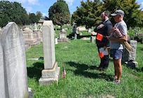 A.J. Orlikoff, Director of Programming at Historic Congressional Cemetery, leads attendees on a guided tour and places a commemorative flag at the final resting place of each identified D.C. Militia member buried at the cemetery in Washington, D.C., Aug. 24, 2026. The tribute honored the Citizen-Soldiers who defended the nation’s capital in 1814 while connecting their legacy of service to the generations who continue that mission today.