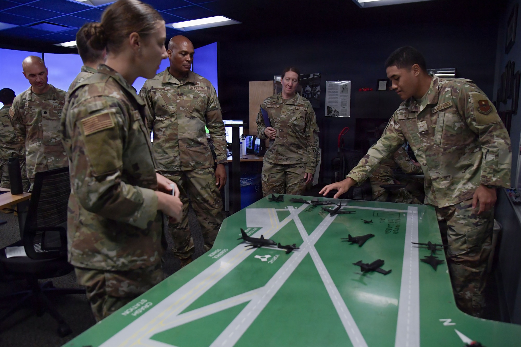People wearing U.S. Air Force uniforms move small hand-held aircrafts on a green table.