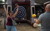A woman celebrates with her arms raised in front of an inflatable axe throwing game