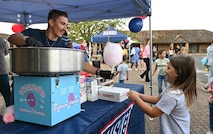 A man in a navy blue shirt hands a young girl in a pink shirt a stick of pink cotton candy