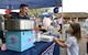 A man in a navy blue shirt hands a young girl in a pink shirt a stick of pink cotton candy
