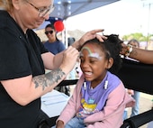 A child gets a rainbow painted on their forehead by a woman wiht a floral tattoo on her arm