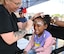 A child gets a rainbow painted on their forehead by a woman wiht a floral tattoo on her arm