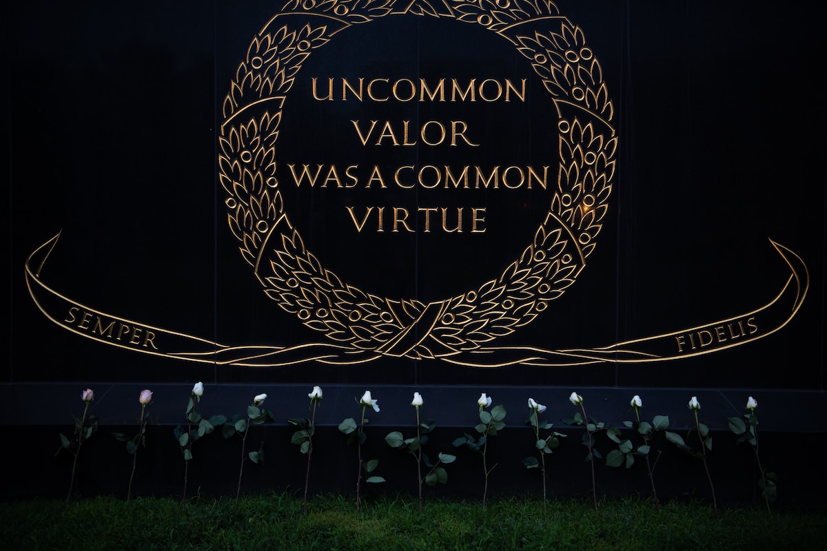 Thirteen roses, two pink and eleven white, rest on a black pedestal.