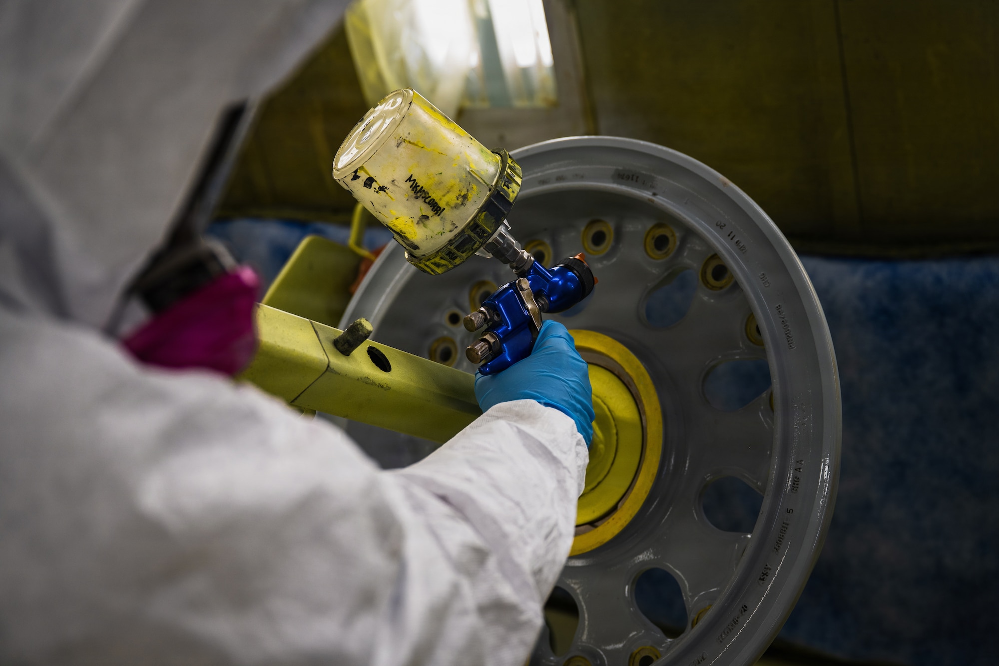 U.S. Air Force Senior Airman Jared Martrano, 22nd Maintenance Squadron aircraft structural maintenance specialist, demonstrates the use of a high-volume, low-pressure paint gun while simulating the refurbishment of a KC-46A Pegasus wheel at McConnell Air Force Base, Kansas, Aug. 24, 2026. The HVLP system delivers paint through a hose and uses compressed air to produce a controlled spray pattern, helping technicians achieve consistent coverage while minimizing overspray. (U.S. Air Force photo by Airman Matthew Nguyen)