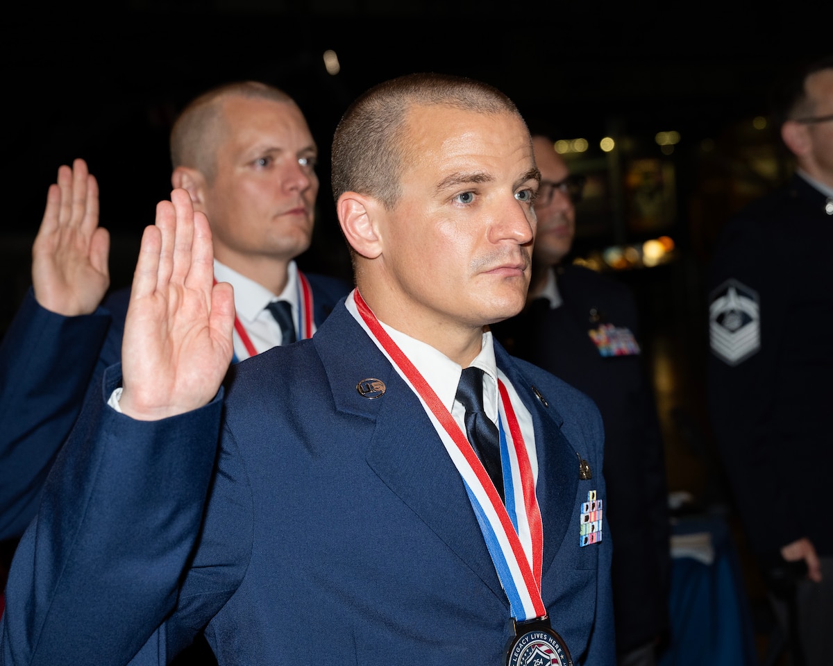 Two men in dress uniform hold their right hands up taking a pledge.