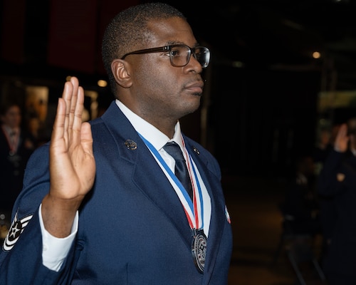 A man in an Air Force dress uniform holds his hand up taking a pledge.
