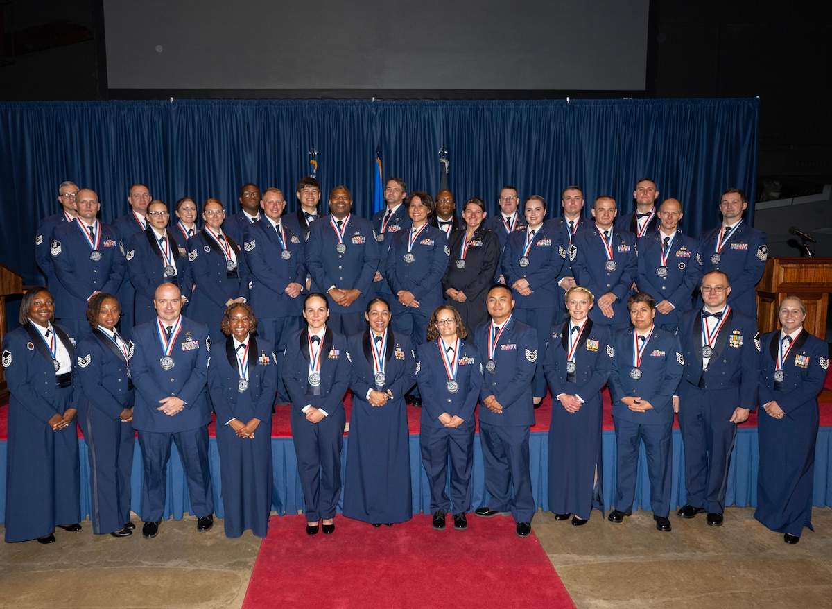 A group of 33 men and women, in dress uniform and wearing medallions, pose for a group photo