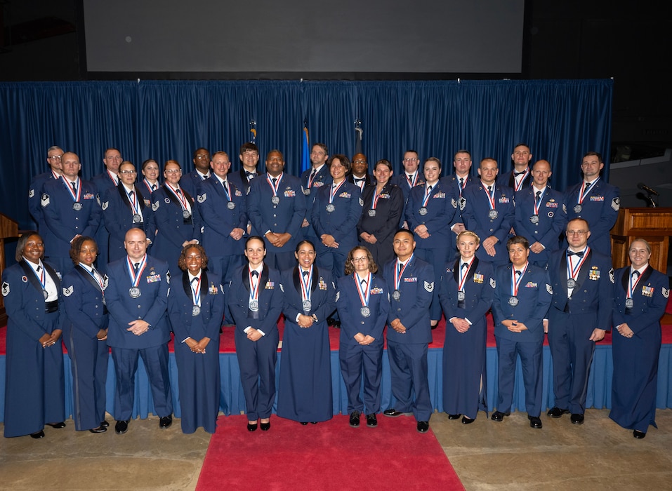 A group of 33 men and women, in dress uniform and wearing medallions, pose for a group photo