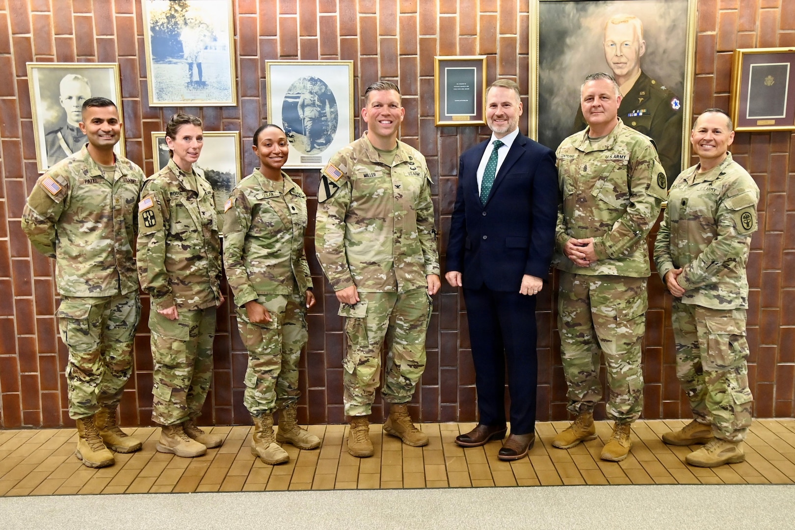 Hospital leaders pose with a guest speaker in front of BJACH's "Wall of Fame."