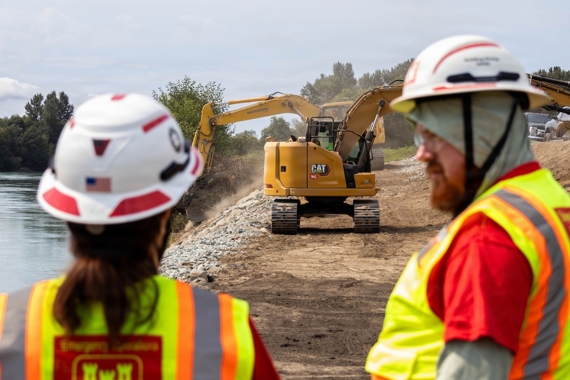 Photo of two people wearing safety gear discussing levee rehabilitation efforts on a levee site.
