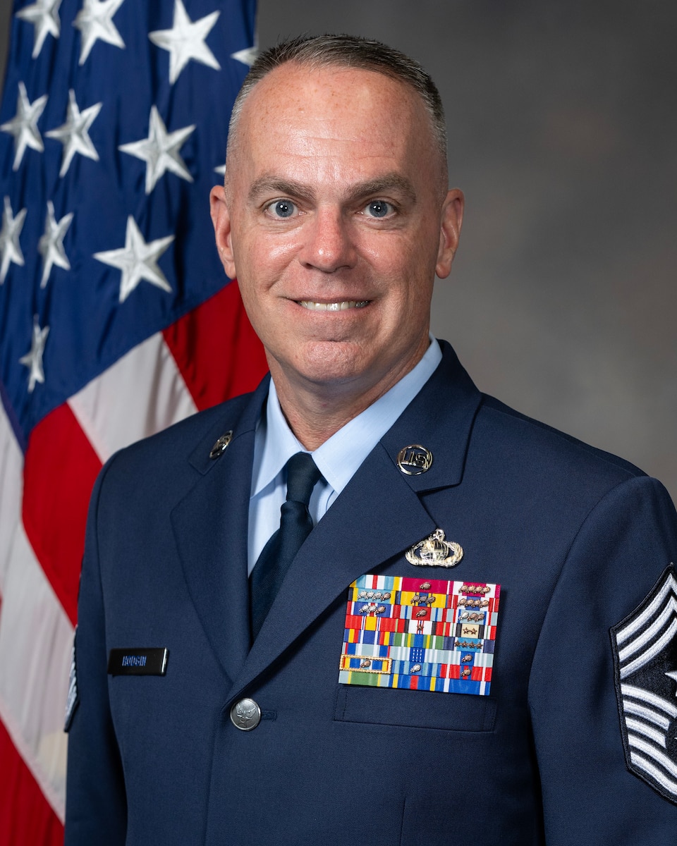 Chief Master Sgt. Timothey C. Hodgin appears looking towards the viewer in full Air Force blues. The American flag is visible over his right shoulder.