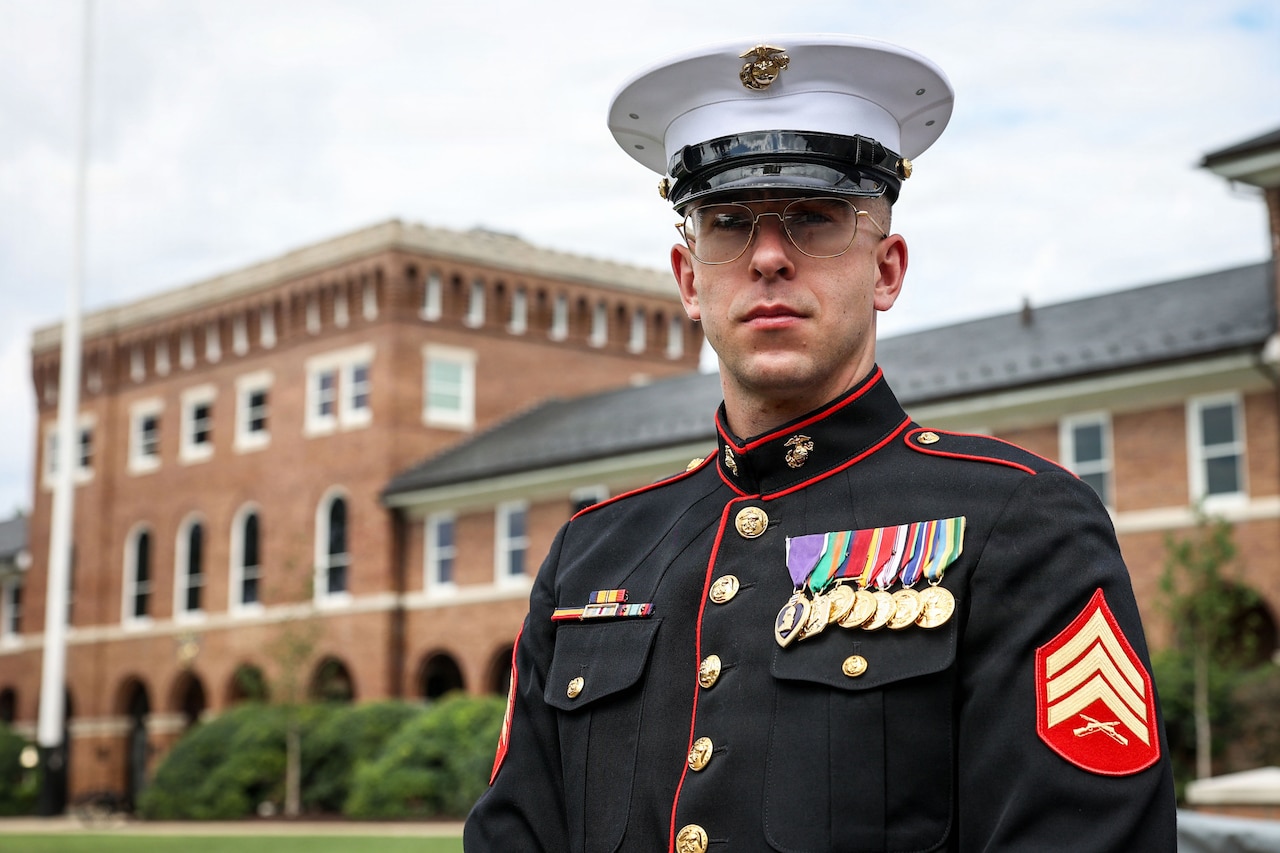A portrait of a man in a formal military uniform outside in front of a large brick building.
