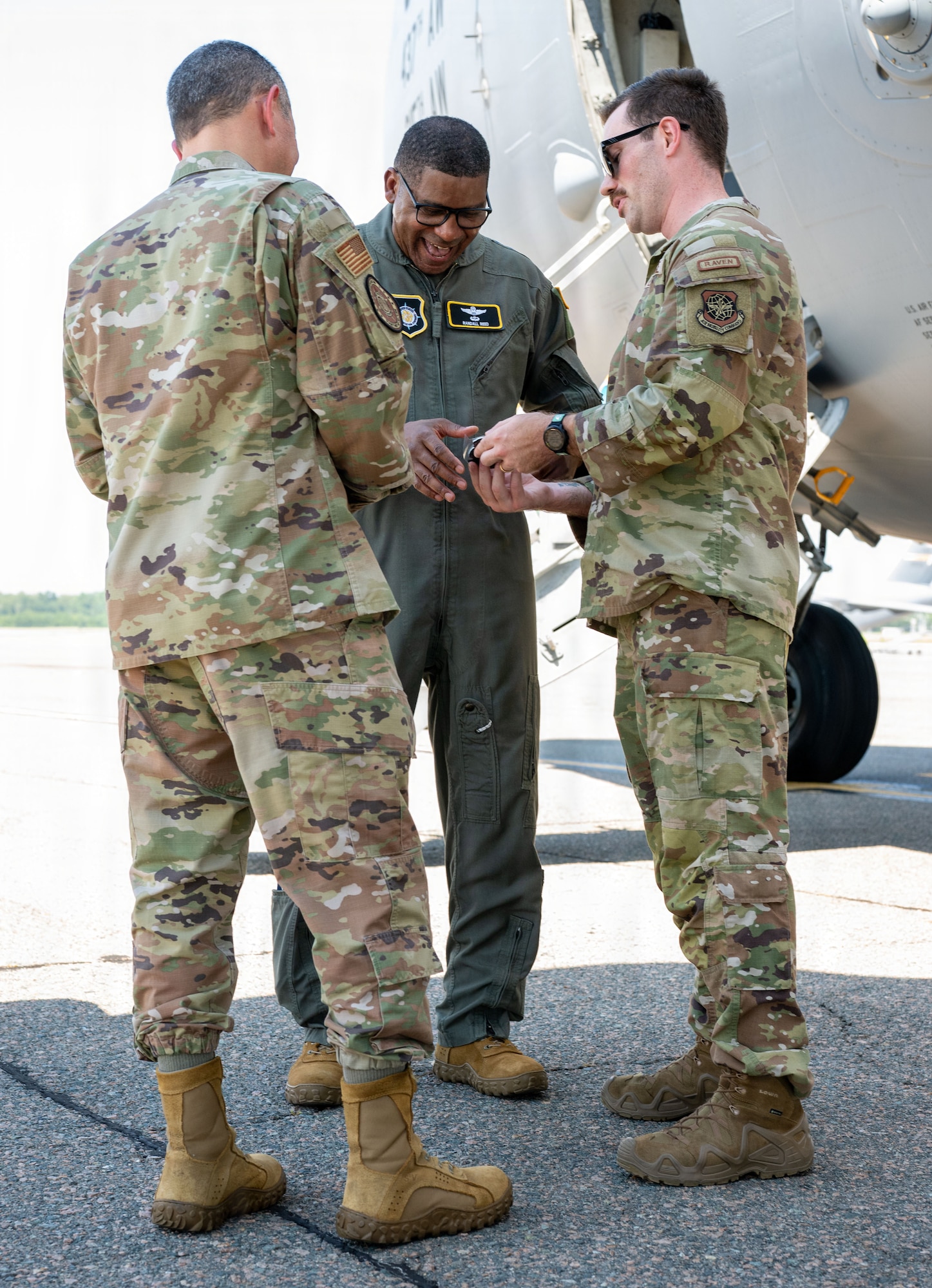 Three people stand together, one receiving a patch from another while standing in front of a C-17 Globemaster III.