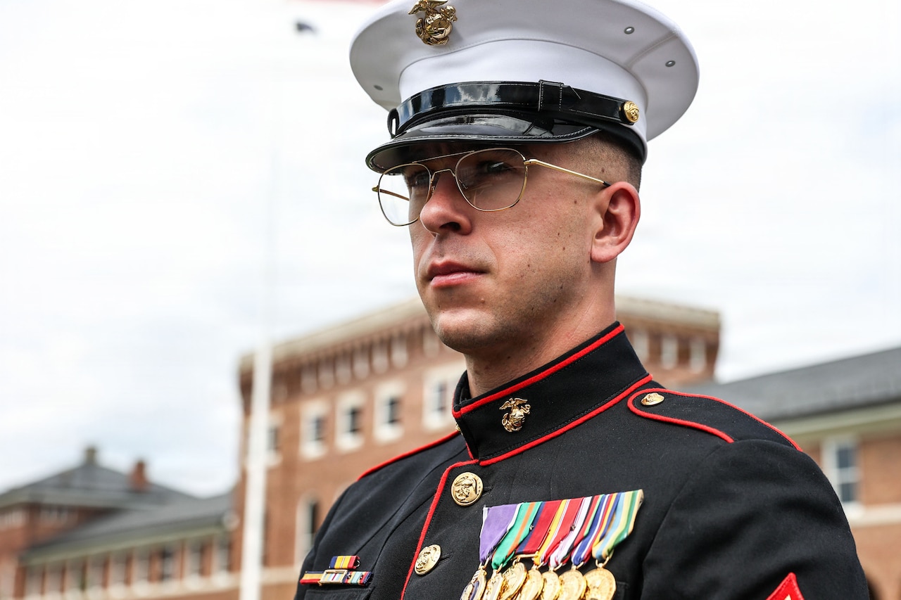 A portrait of a man in a formal military uniform outside in front of a large brick building.