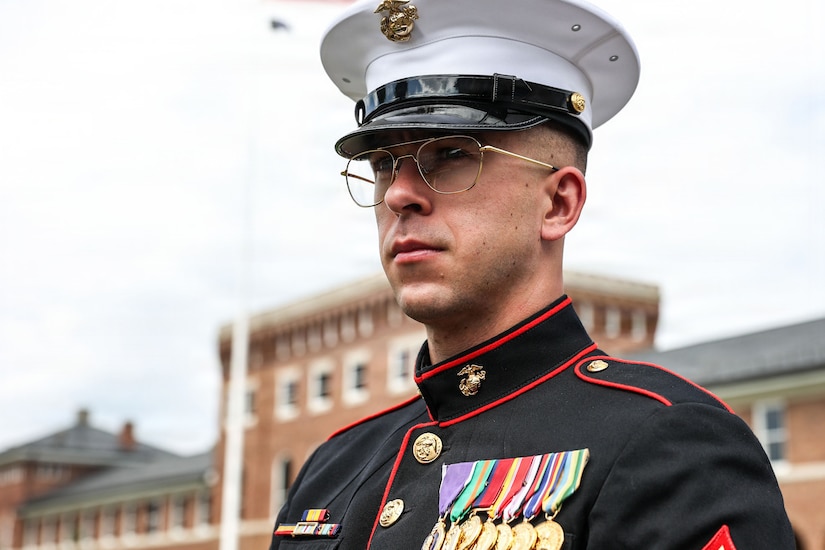 A portrait of a man in a formal military uniform outside in front of a large brick building.
