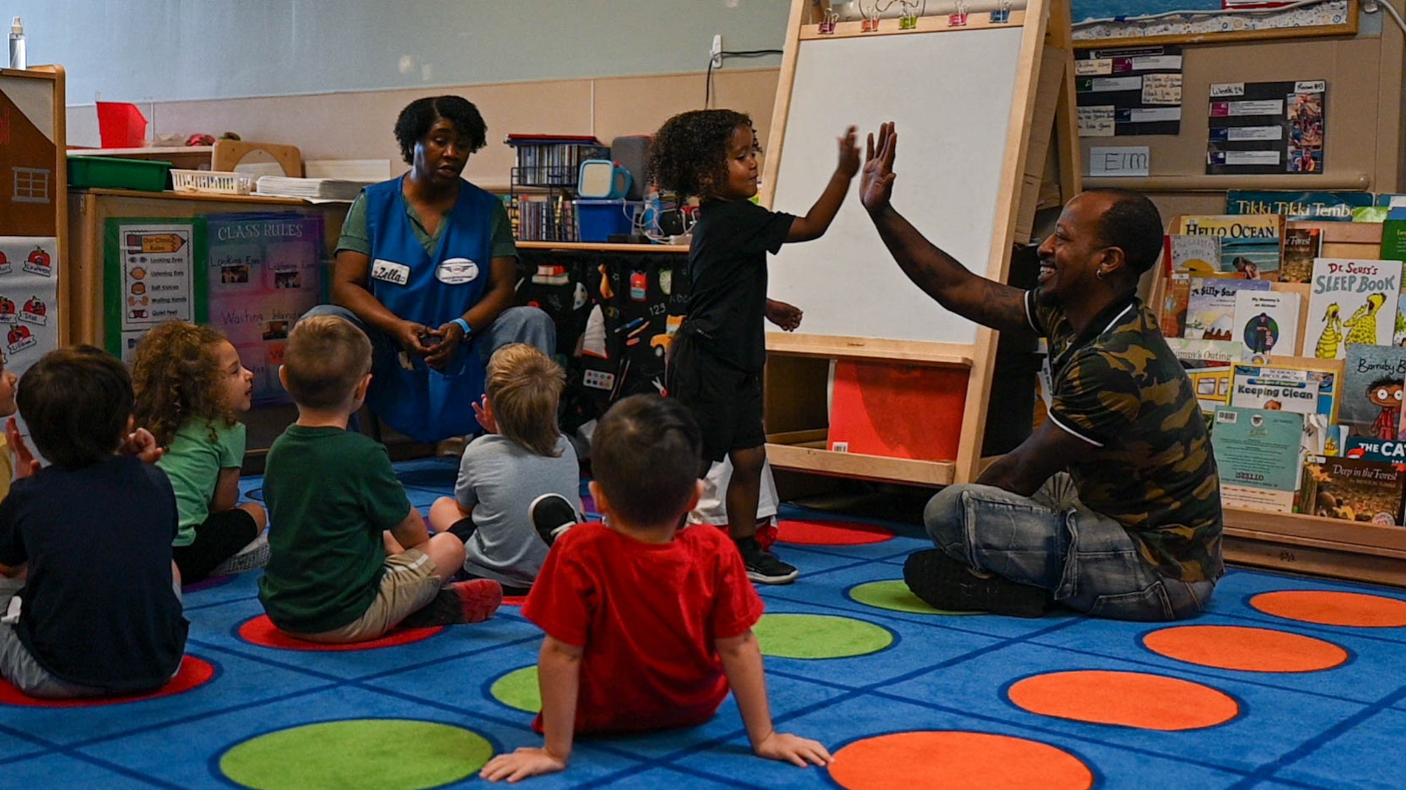 A man high fives a child while sitting with a group of children.