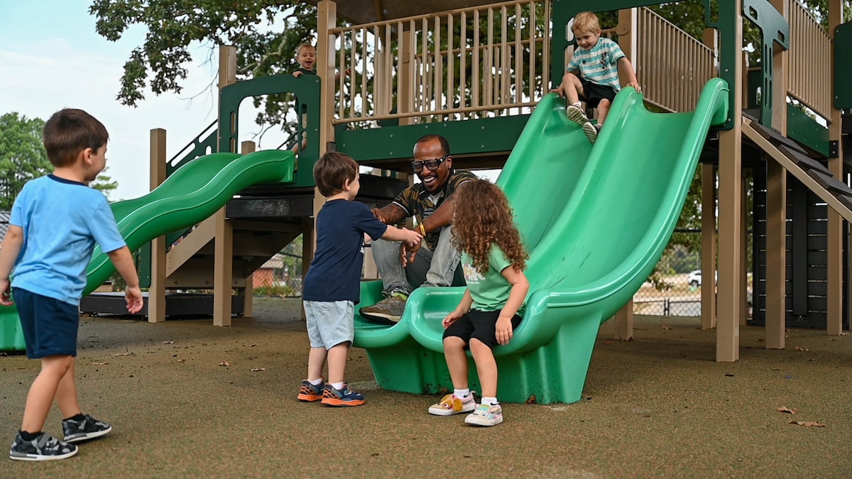 A man interacts with children on a slide.
