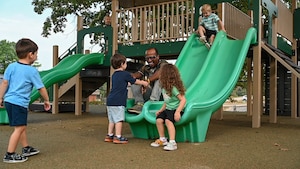 A man interacts with children on a slide.
