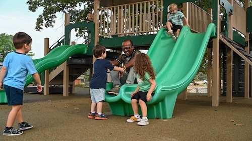 A man interacts with children on a slide.