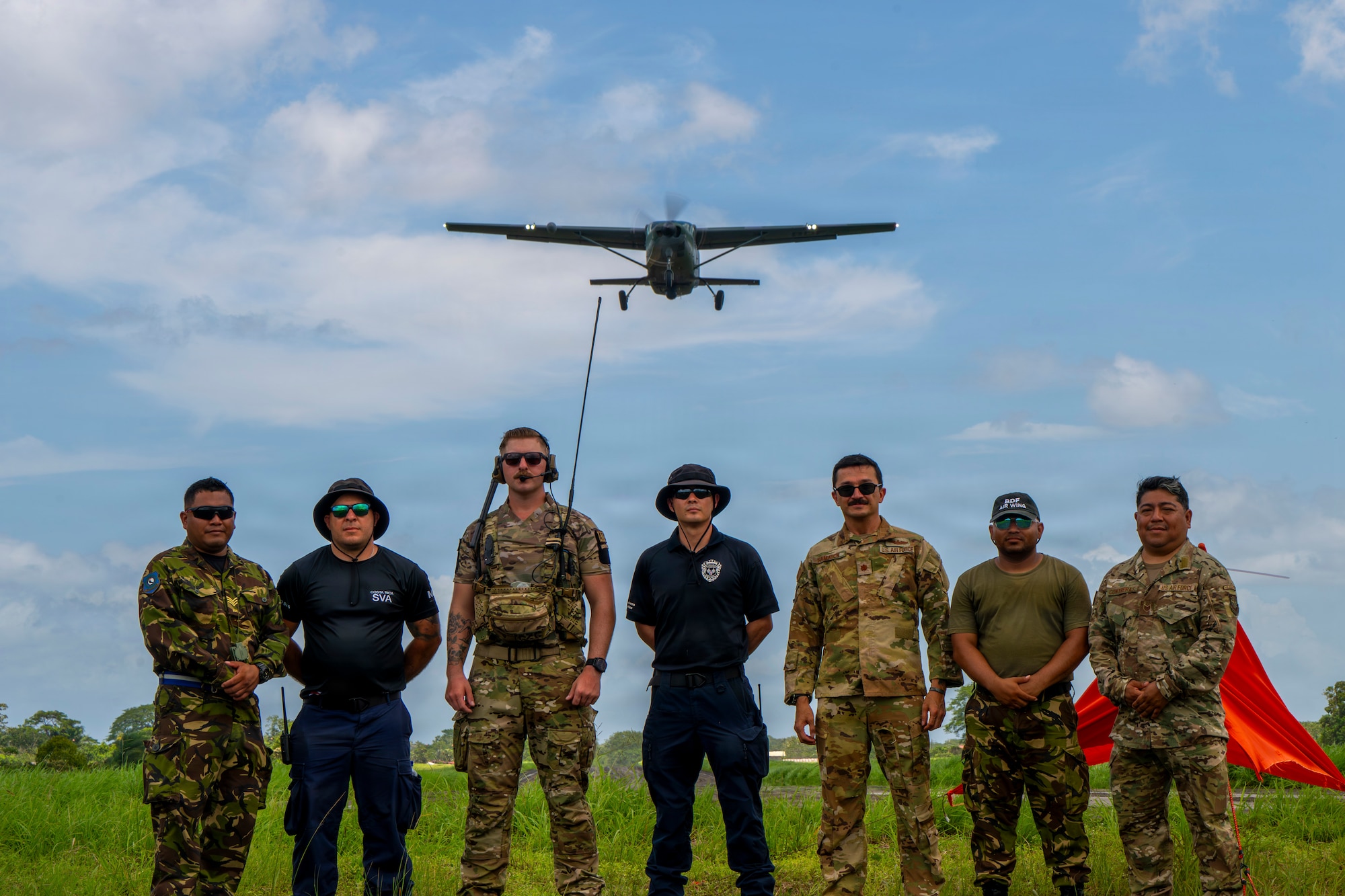 Men stand for a photo as a plane flies overhead.
