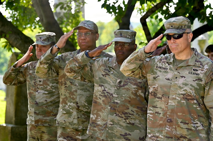 Four men dressed in camouflage military uniforms render a salute.