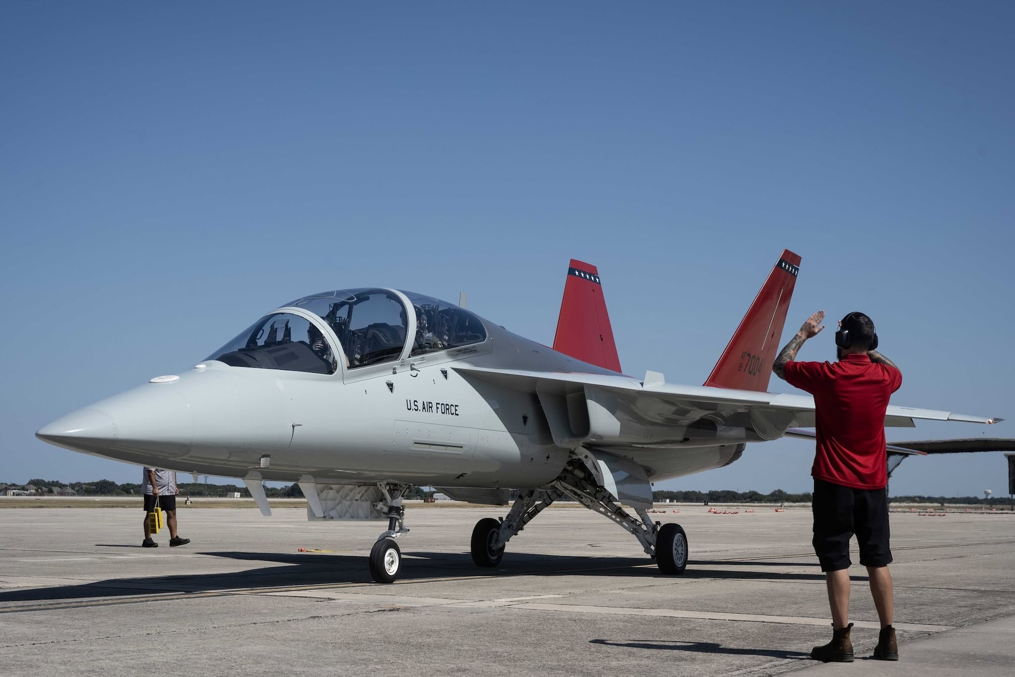 A T-7A Red Hawk is marshalled in on a runway.