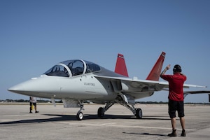 A T-7A Red Hawk is marshalled in on a runway.