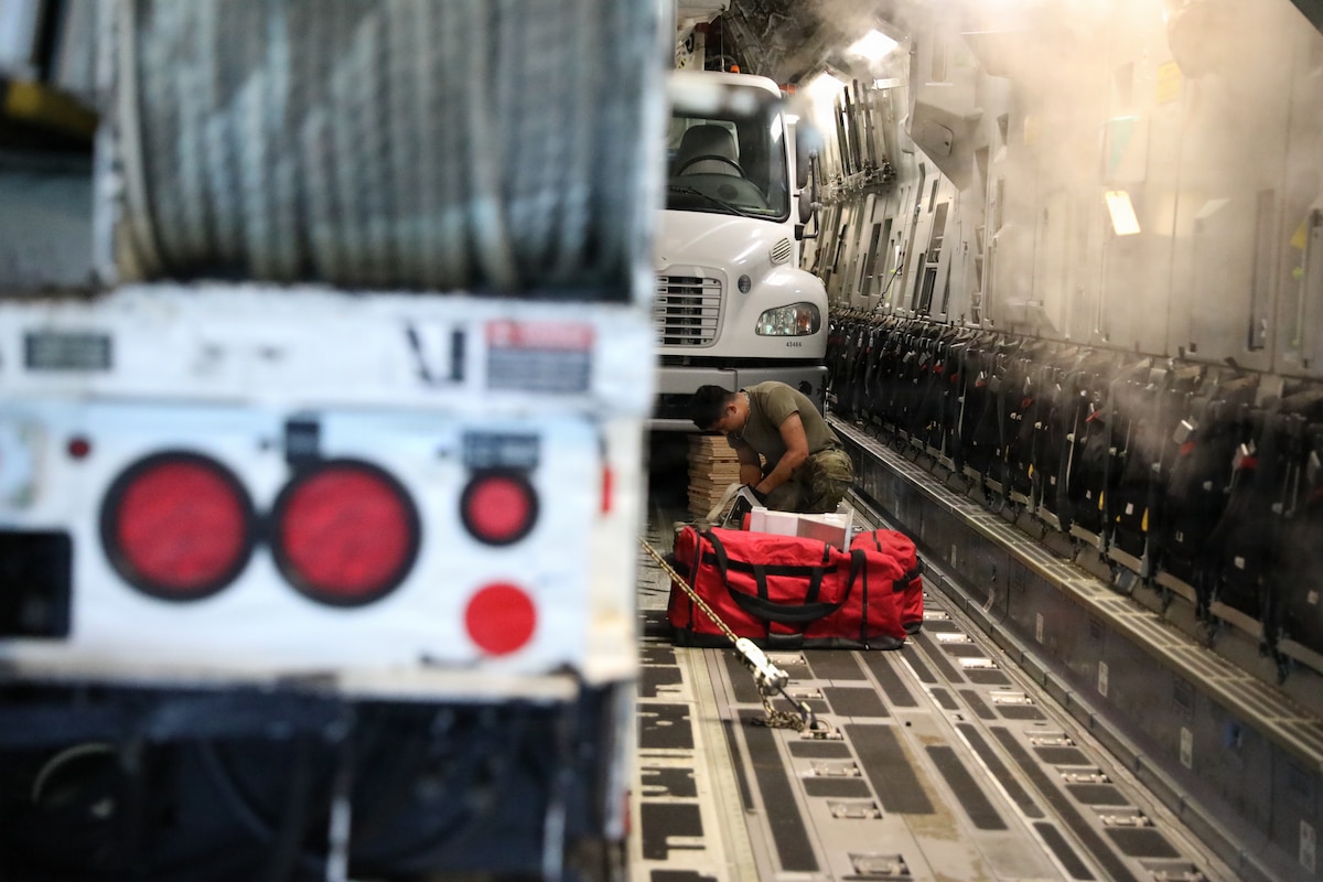 Photo of a loadmaster securing a truck inside a C-17