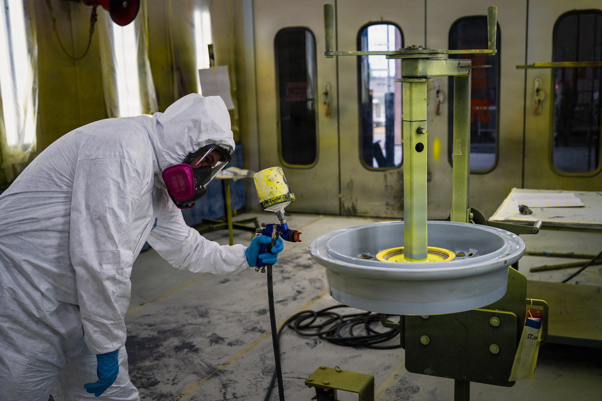 U.S. Air Force Senior Airman Jared Martrano, 22nd Maintenance Squadron aircraft structural maintenance specialist, simulates painting a KC-46A Pegasus wheel while wearing personal protective equipment at McConnell Air Force Base, Kansas, Aug. 24, 2026. Aircraft coatings and primers can contain hazardous substances such as hexavalent chromium, making respiratory protection, gloves, eye protection and protective clothing essential for limiting exposure during painting operations. Environmental Protection Agency regulations and other exposure-control measures help reduce the release of toxic substances into the atmosphere and protect personnel working with hazardous aircraft coatings. (U.S. Air Force photo by Airman Matthew Nguyen)