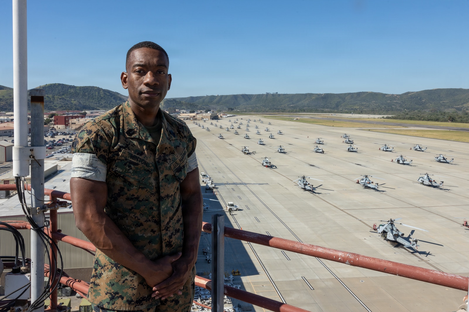 U.S. Marine Corps Master Sgt. poses for a photo in front of a flightline with helicopters staged in lines.