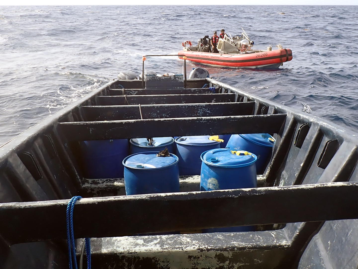 Empty suspected drug smuggling vessel with a Coast Guard small boat in the background.