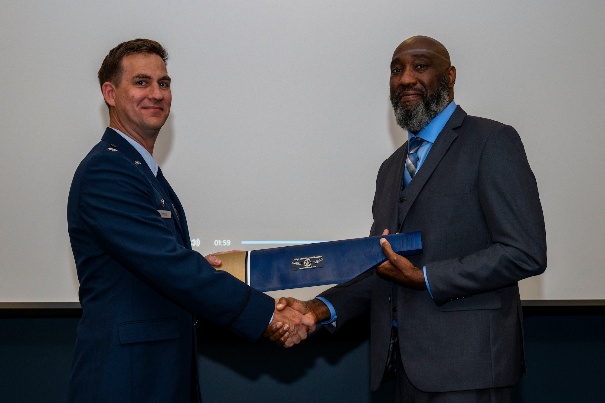 2 men shake hands and hold an award.