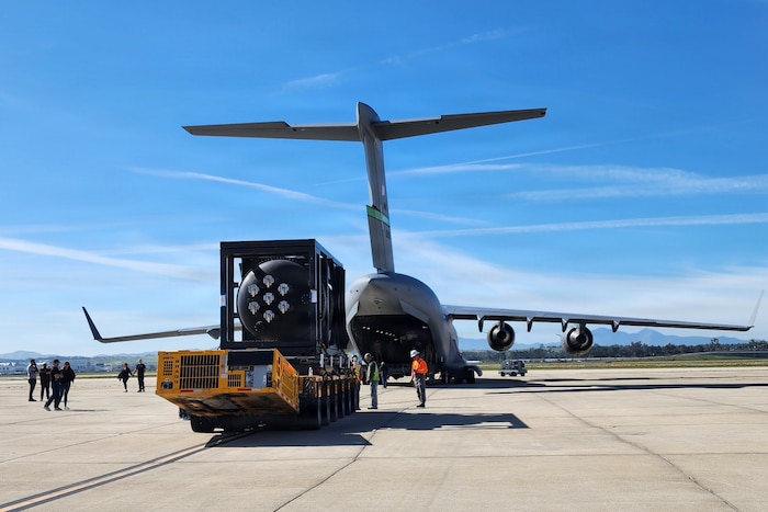 A nuclear reactor is transported across a tarmac to a military aircraft with the loading bay boor open.