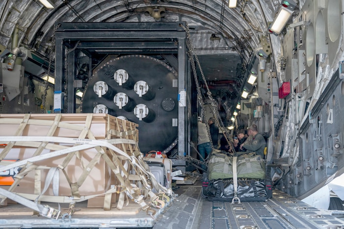 A nuclear reactor and other equipment are strapped into the loading bay of a military aircraft.