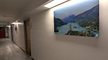 A photo of a renovated hallway in an Unaccompanied Housing (UH) building – commonly known as barracks – on Naval Base Kitsap-Bremerton. The 10-story, 152-room barracks received full-scale interior renovation and new furnishing following fire and water damage sustained in August 2025. The milestone marks the first of the Navy’s six major sustainment, restoration, and modernization projects funded through the Barracks Task Force to reach completion, directly advancing the Navy’s “No Sailor Living Afloat” initiative – a drive to move Sailors off docked ships and into high-quality shore housing – and the Commander, Navy Installations Command (CNIC) Quality of Service improvement efforts.