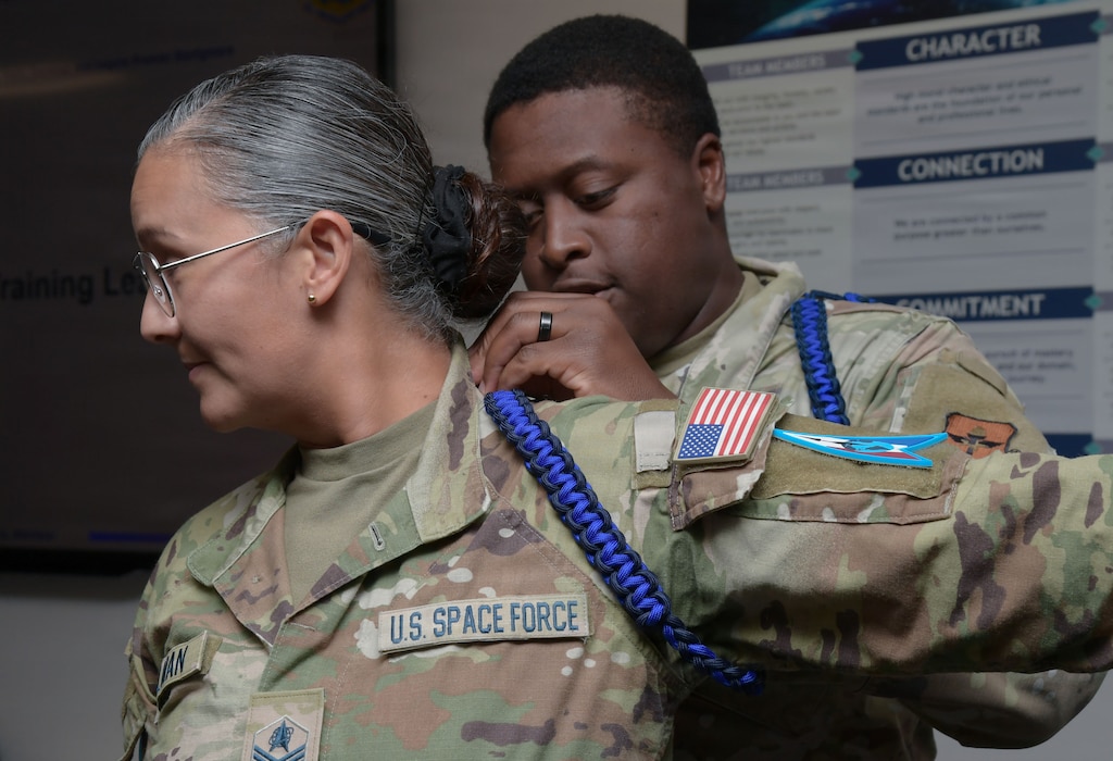 A U.S. Airman places an aiguilette on the arm of a U.S. Space Force Guardian.
