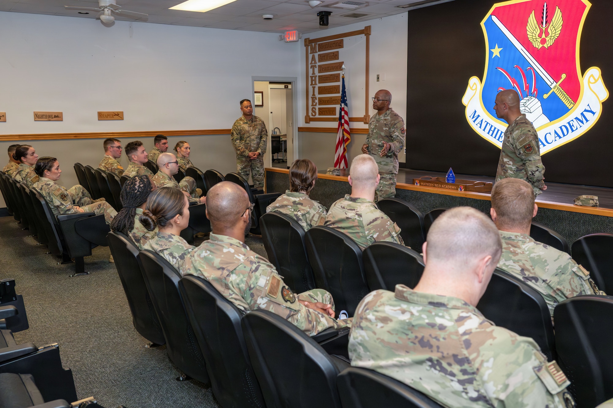 U.S Air Force Airmen speak to a group of Airmen inside a auditorium.