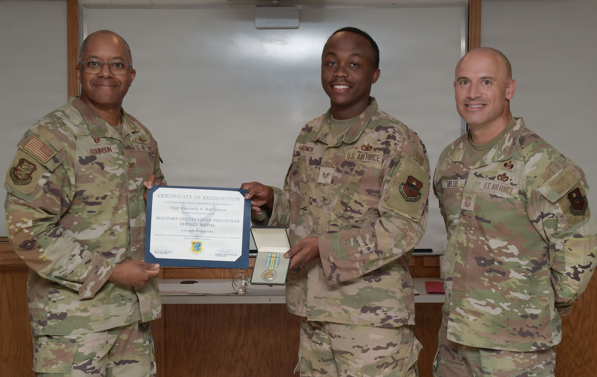 Three U.S. Air Force Airmen pose for a photo while holding a certificate and medal.