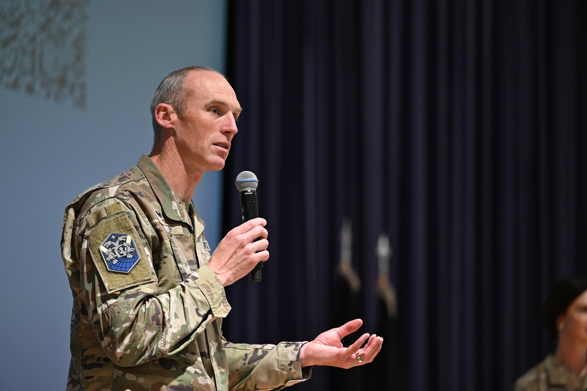 Col. Cooper holds a microphone as he addresses the audience.