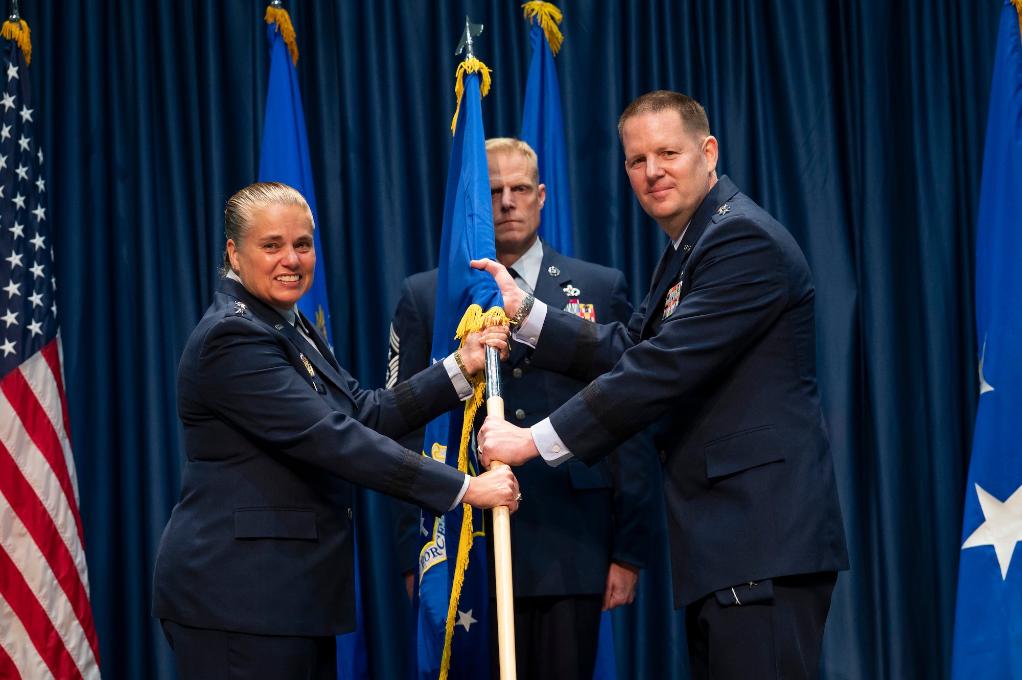 Female 3 star Air Force general handing AFLCMC flag to a male 3 star Air Force general.