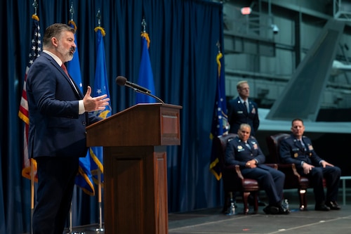 Man in blue jacket giving speech behind wood podium.