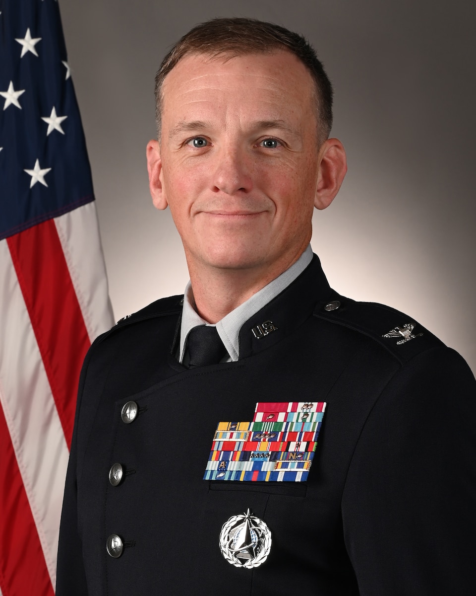 A man in uniform poses in front of an American flag.