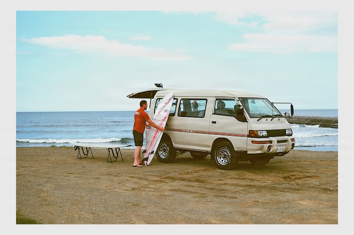 Craig Hale, Nick Pallett’s friend, unloads a surfboard on a beach.