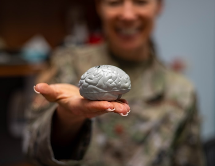 A female airman holds up a grey model of a small human brain.