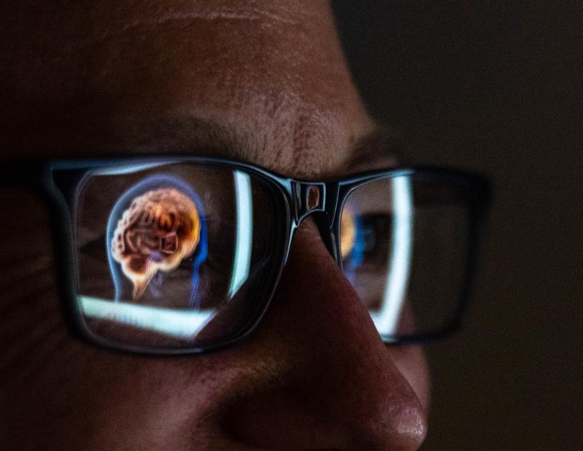 A close up of a woman in glasses looking at a picture of a human brain being reflecting in her glasses.