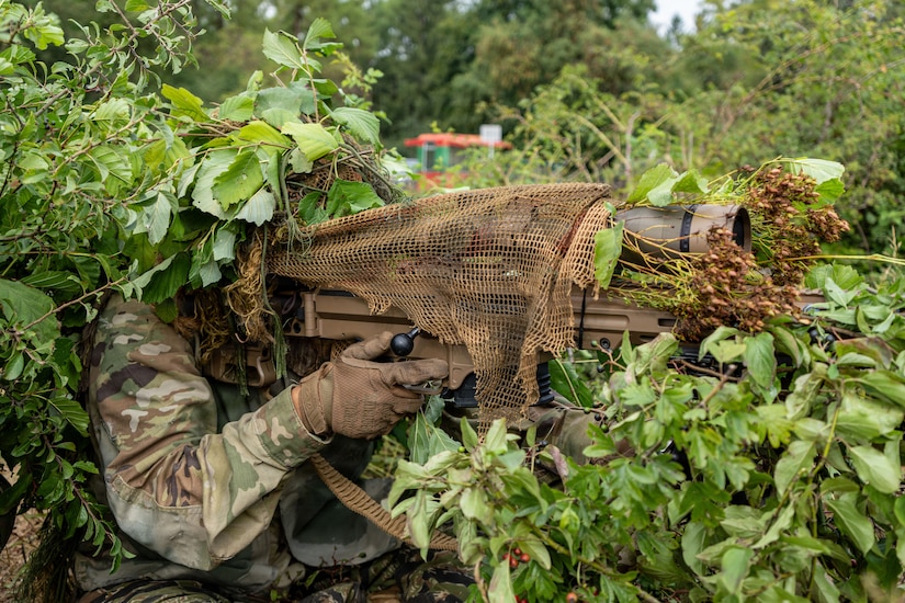 Two people wearing military combat gear walk through a forest.