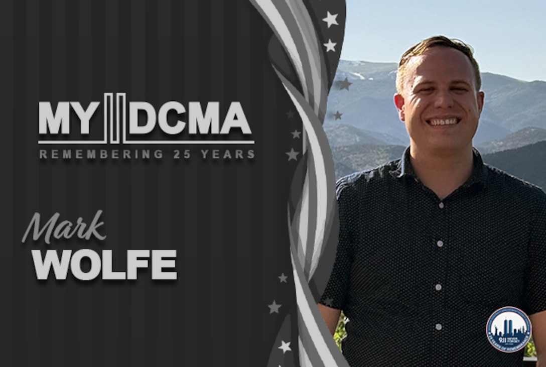 Smiling man wearing a black shirt stands in front of mountains