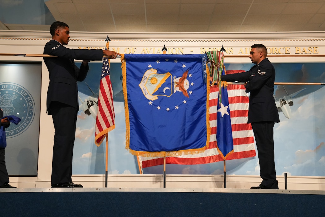 an airman unfurls a blue flag in front of another flag that is being furled behind it